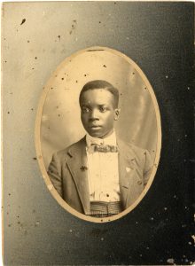 black and white mounted photograph of a young boy in a suit and bow tie