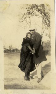 black and white photograph of a couple posing as if dancing, outside in a field and wearing nice clothing