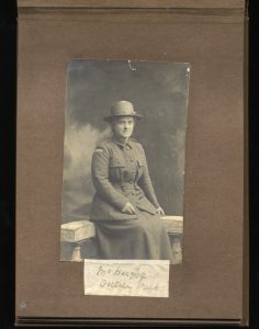 scanned image of a scrapbook page with a photo of a woman in a WWI uniform seated on a bench with a caption of her name below