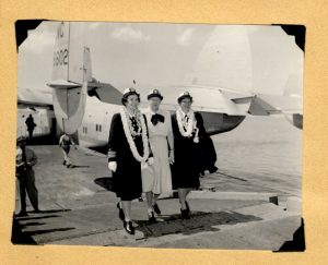 scanned image of a photograph of three women in uniform wearing leis, standing in front of an airplane